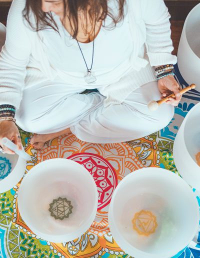 Woman in white attire playing crystal singing bowls.