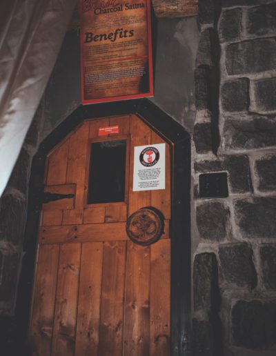 Wooden door entrance to Black Charcoal Sauna with sign above.