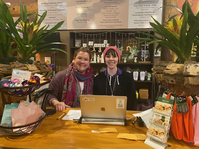 Staff at boutique checkout counter smiling behind laptop.