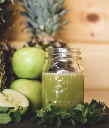 Green apple juice beside fresh ingredients.